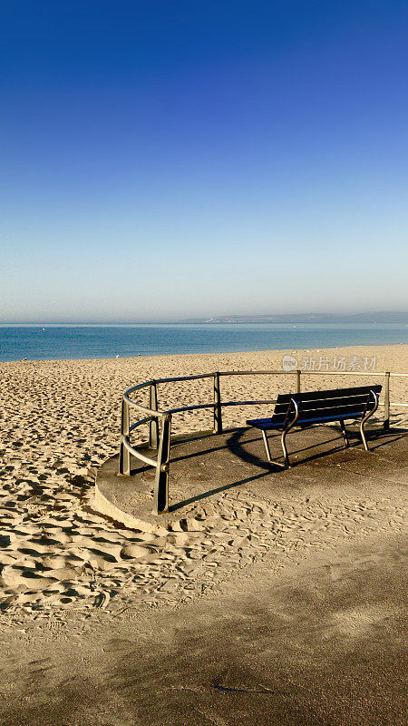 英国多塞特郡伯恩茅斯海滩/普尔沙洲的海滨长椅，俯瞰平静的大海、阳光明媚的蓝天和金色的沙滩，配有金属和木制的长椅，供在英国海边度假的游客坐下来欣赏美景
